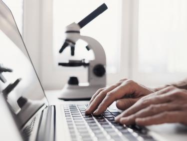 Person arbeitet an einem Laptop mit Mikroskop im Hintergrund